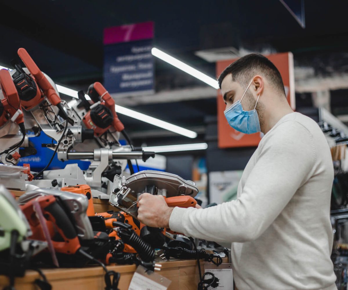 young-man-in-mask-choosing-circular-saw-in-hardwar-4KHH73N.jpg